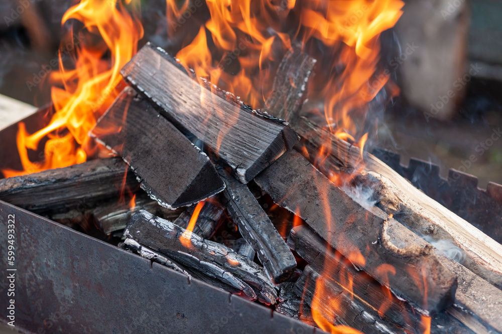 The firewood in the grill burns with a bright orange flame. Preparation for cooking meat on the grill in nature. Fire flames and smoke The firewood in the grill burns with a bright orange flame. Preparation for cooking meat on the grill in nature. Fire flames and smoke