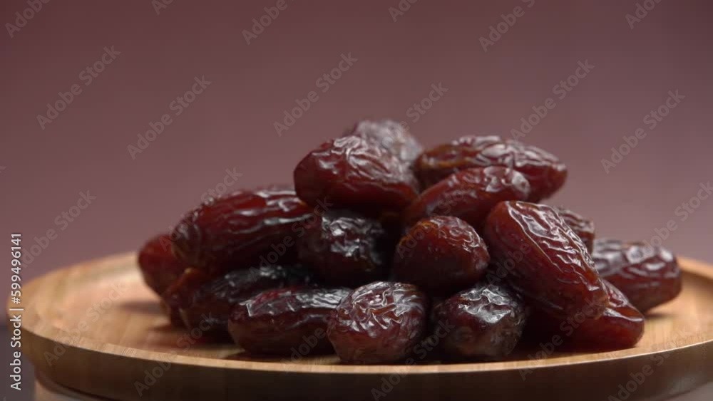 A pile of ripe dates are spinning on a wooden cup. A hand takes a date from the cup. A pile of ripe dates are spinning on a wooden cup. A hand takes a date from the cup.