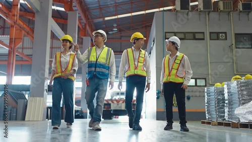 Group of Asian warehouse workers in safety uniform having discussion while walking through industry manufacturing factory. Factory warehouse concept