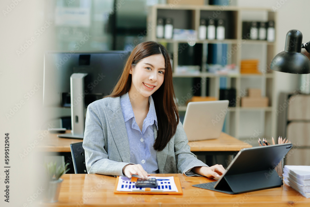 Confident Asian woman with a smile standing holding notepad and tablet at the modern office..