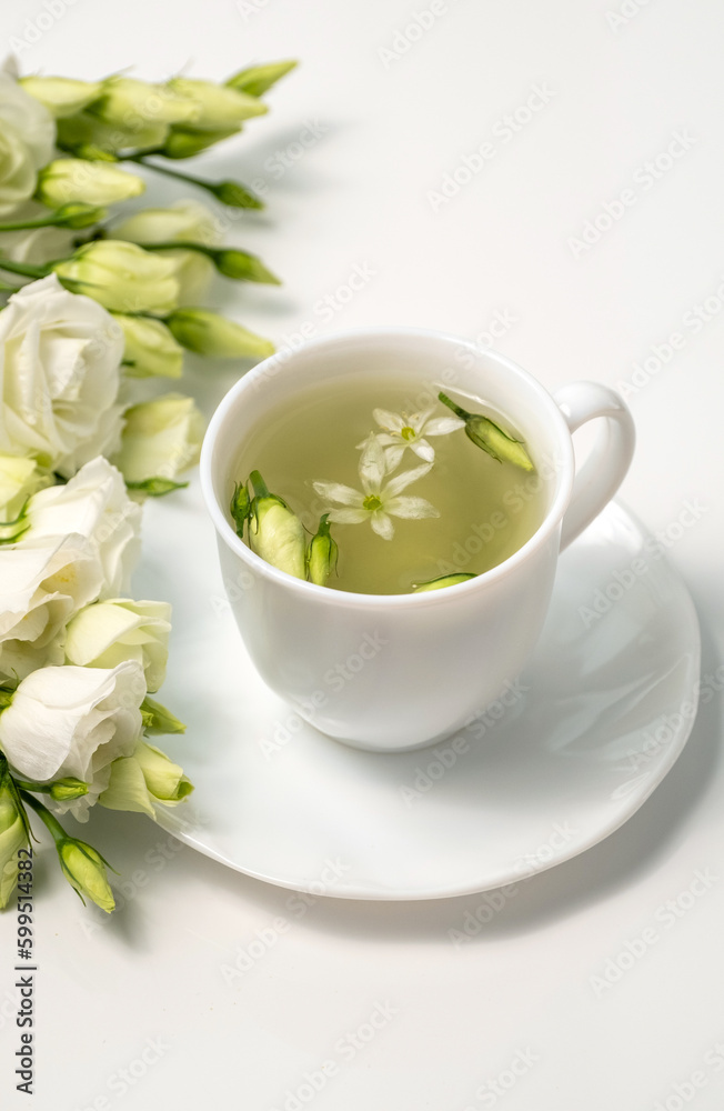 Floral tea. White cup with fragrant herbal tea and Eustoma Lisianthus flowers near. Tea time. Relaxing with herbal tea, white background, top view, vertical Floral tea. White cup with fragrant herbal tea and Eustoma Lisianthus flowers near. Tea time. Relaxing with herbal tea, white background, top view, vertical