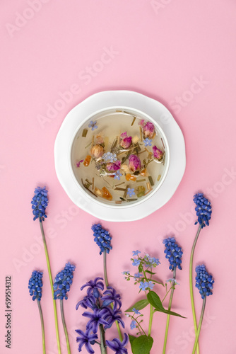 Healthy herbal tea in a white cup with medicinal herbs, spring flowers and Chinese tea rose buds Mei Gui Hua for relaxation and wellness. Floral Infusion, top view, vertical