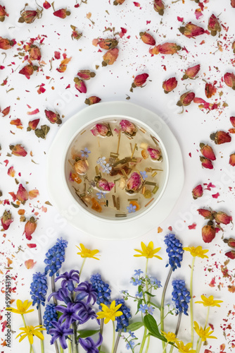Healthy herbal tea in a white cup with medicinal herbs, spring flowers and Chinese tea rose buds Mei Gui Hua for relaxation and wellness. Floral Infusion, top view, vertical