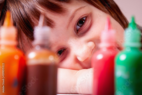 Close up portrait of happy young girl in front of multicolored paints. Art, childhood, color, and creativity concept.