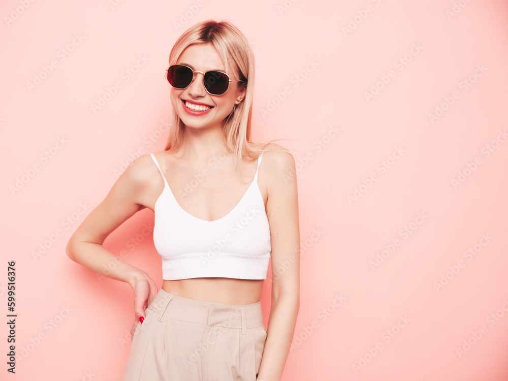 Young beautiful smiling blond female in trendy summer white top t-shirt and beige trousers clothes. Sexy carefree woman isolated on pink background in studio. Positive model having fun. Sunglasses Young beautiful smiling blond female in trendy summer white top t-shirt and beige trousers clothes. Sexy carefree woman isolated on pink background in studio. Positive model having fun. Sunglasses