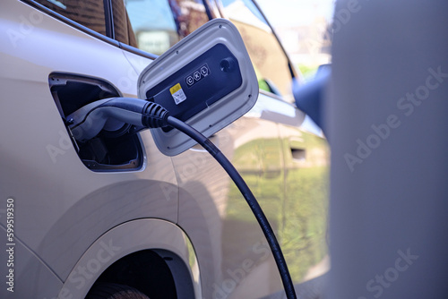 Close up of a white electric car being charged by a charging station