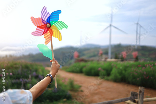 An ordinary woman raises her hand with a small wind turbine among large wind turbines producing clean and non-polluting energy. Wind power electric energy concept