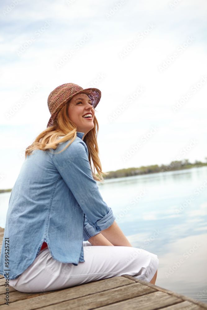 Relaxing by the waters edge. A happy young woman sitting on a jetty next to a lake.