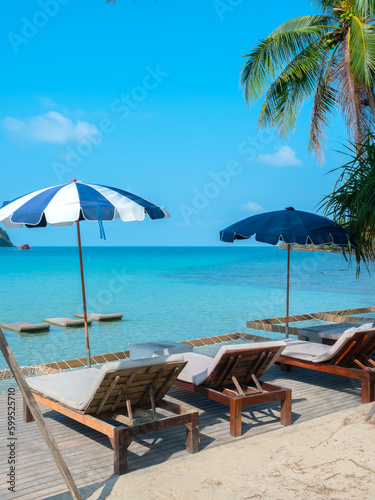 Two wooden sunbeds with bed pads decoration with blue striped standing beach umbrella on seascape scene with blue sea ocean and summer sky background, vertical. Holiday travel vacation background.