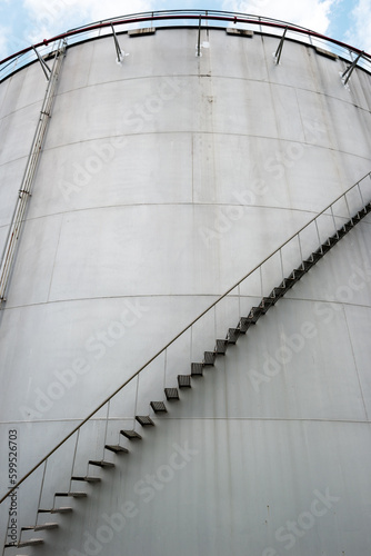 Industrial tanks for petrol and oil with blue sky. Fuel tanks at the tank farm close up. Metal stairs on the side of an industrial oil container. Staircase on big fuel tank.