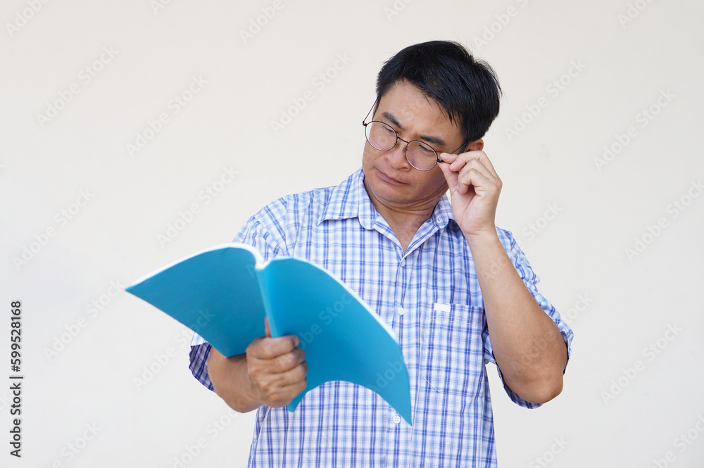 Asian middle aged man wears eyeglasses is reading book. Concept , Eyesight health problem. Optometry. Glasses with convex or concave lenses. Myopia.Eye disease. Asian middle aged man wears eyeglasses is reading book. Concept , Eyesight health problem. Optometry. Glasses with convex or concave lenses. Myopia.Eye disease.