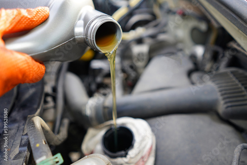 Pouring oil to the car. Car mechanic holding a bottle of oil in hand over the engine. Car engine oil. Topping up car oil.