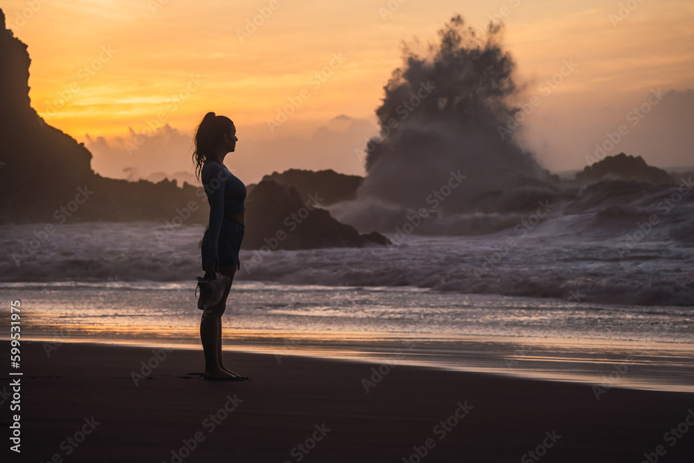 woman walking on the beach with her shoes in her hand while looking at the sea. sunset on the island of tenerife Spain