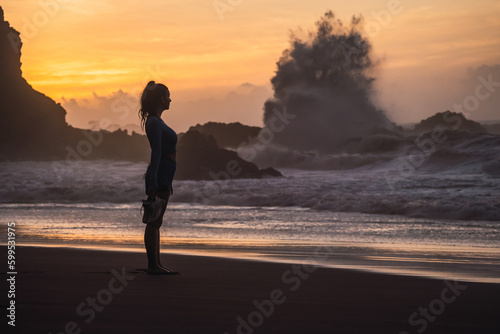 Obraz na płótnie woman walking on the beach with her shoes in her hand while looking at the sea. sunset on the island of tenerife Spain w salonie