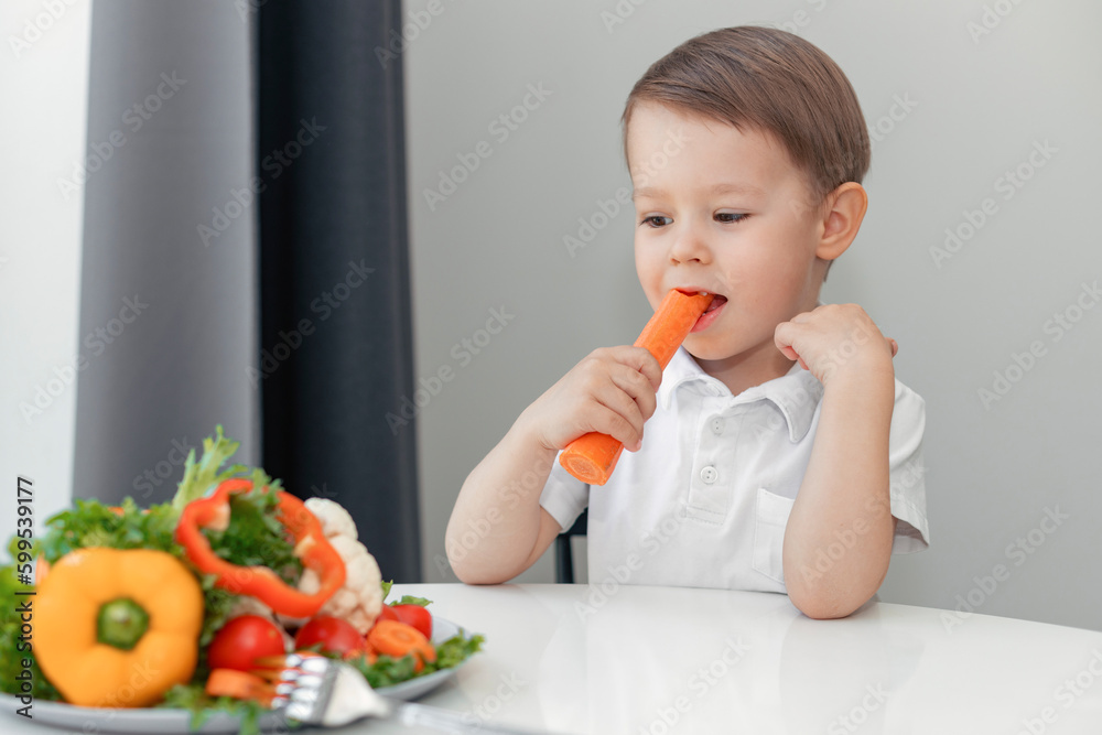 boy with appetite eats carrots and fresh vegetables at the table at home, the concept of a healthy diet for children