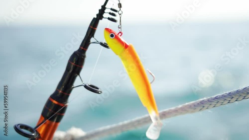 Plastic yellow-red fishing lure on a fishing rod close-up. Wobbler. Fishing in the sea. Fast sailing on a sailboat. 4К