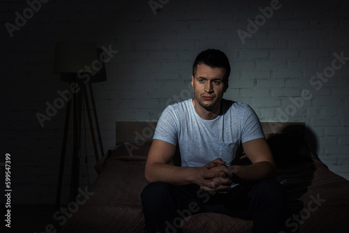 depressed man in white t-shirt sitting on bed while suffering from ptsd.
