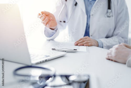 Doctor and patient discussing current health questions while sitting at the table in clinic office, only hands closeup. Medicine concept