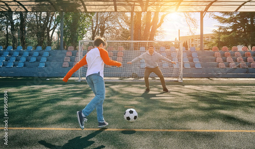 Father and Son play football on stadium outdoors, Happy family bonding, fun, players in soccer in dynamic action playing in sunny day, holidays time. 