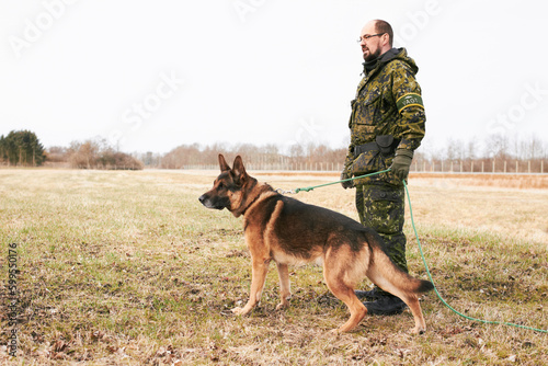 Male officer, military uniform and german shepherd on leash or dog guarding territory and outdoors. Soldier, pet with rope and in the field for army training or drills or man official in gear outside © Fannie H/peopleimages.com