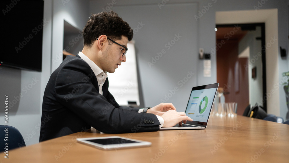 A businessman uses a laptop, a young successful entrepreneur, alone in the office, working in formal clothes.
