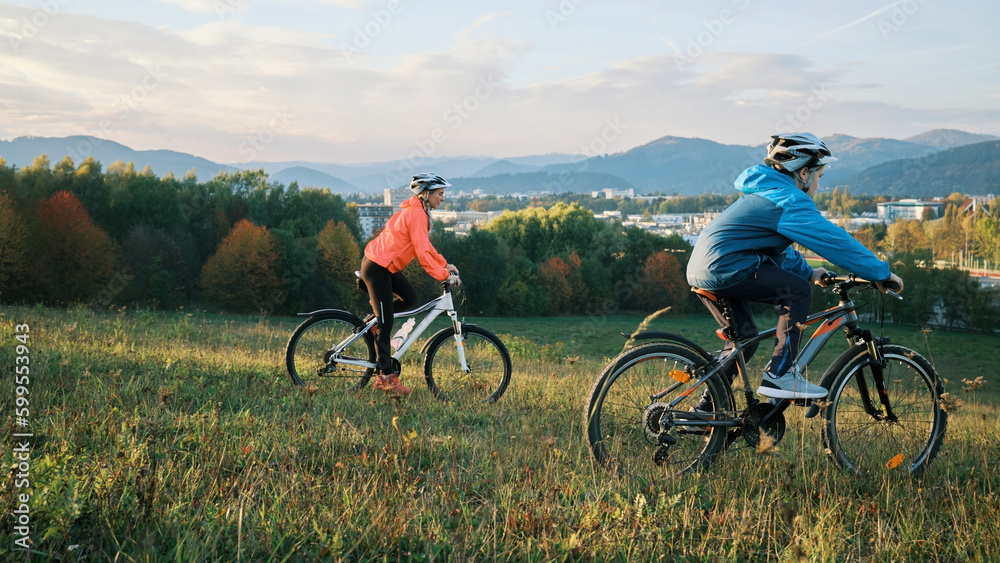 Obraz premium Mother and son ride bike outdoors. Happy cute boy in helmet to riding a bike in park on green meadow at sunset time. Family weekend. mothers Day