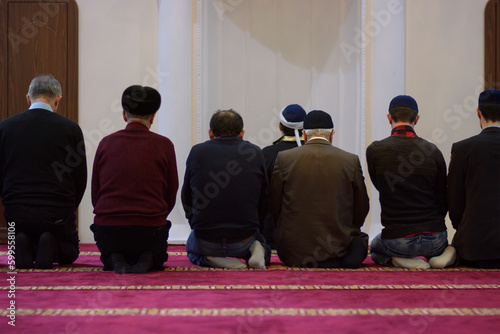 Group of Muslim men and mullah kneeling and praying in a mosque photo
