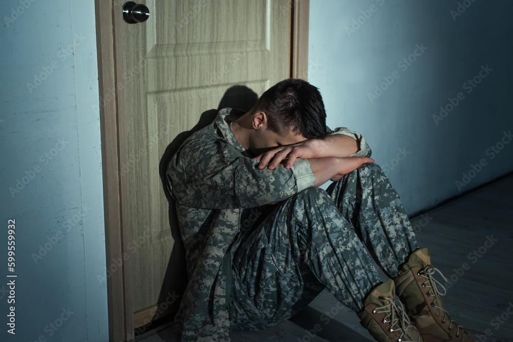 Military man with emotional distress sitting near door in hallway at home at night. Military man with emotional distress sitting near door in hallway at home at night.