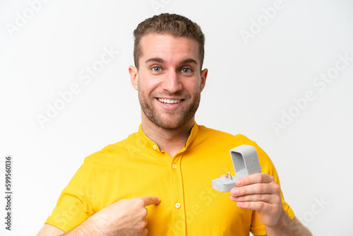 Young man holding a engagement ring isolated on white background with surprise facial expression