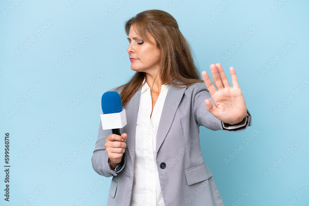 Middle-aged TV presenter woman over isolated blue background making stop gesture and disappointed Middle-aged TV presenter woman over isolated blue background making stop gesture and disappointed