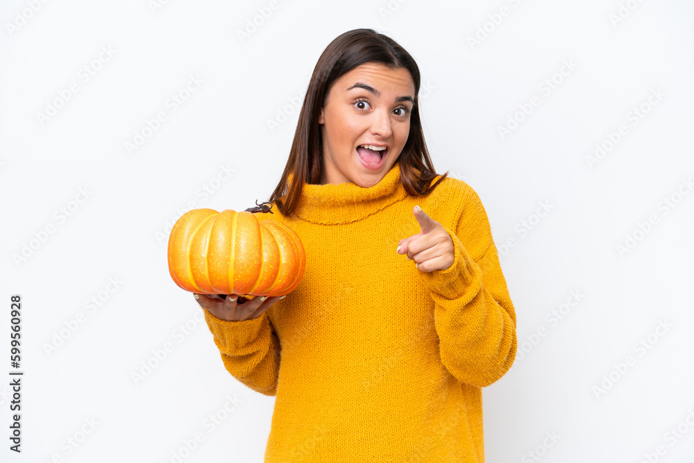 Young caucasian woman holding a pumpkin isolated on white background surprised and pointing front Young caucasian woman holding a pumpkin isolated on white background surprised and pointing front