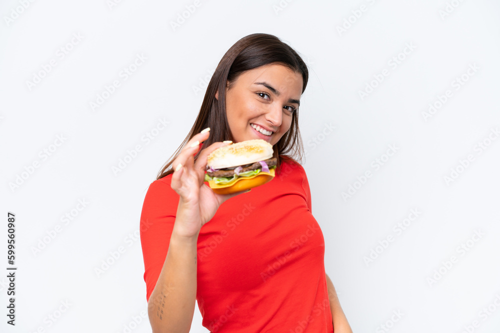 Young caucasian woman holding a burger isolated on white background with happy expression Young caucasian woman holding a burger isolated on white background with happy expression