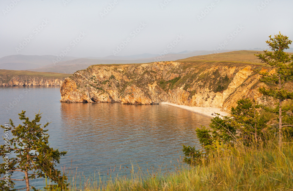 Picturesque landscape of Baikal Lake at sunset. Top view of the sandy beach of the cozy bay of Olkhon Island on a foggy hot evening. Summer travel, hiking and outdoor recreation