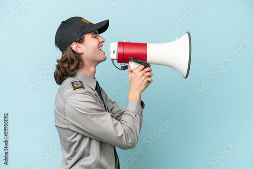 Young safeguard man isolated on blue background shouting through a megaphone
