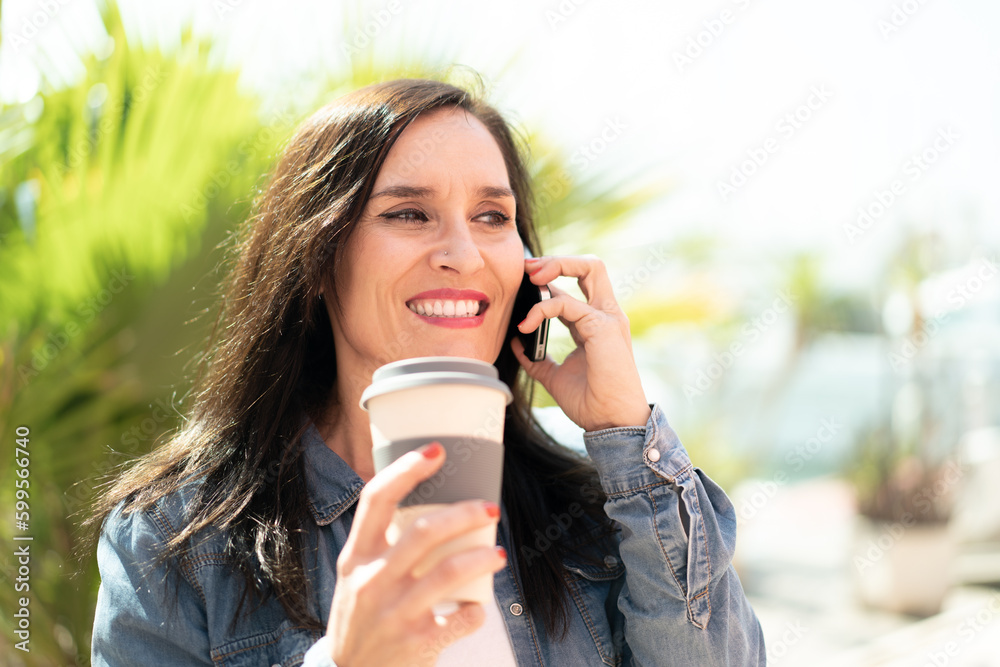 Middle aged woman using mobile phone and holding a coffee with happy expression Middle aged woman using mobile phone and holding a coffee with happy expression
