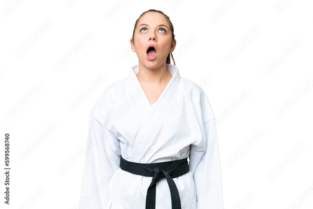 Young blonde woman doing karate over isolated chroma key background looking up and with surprised expression