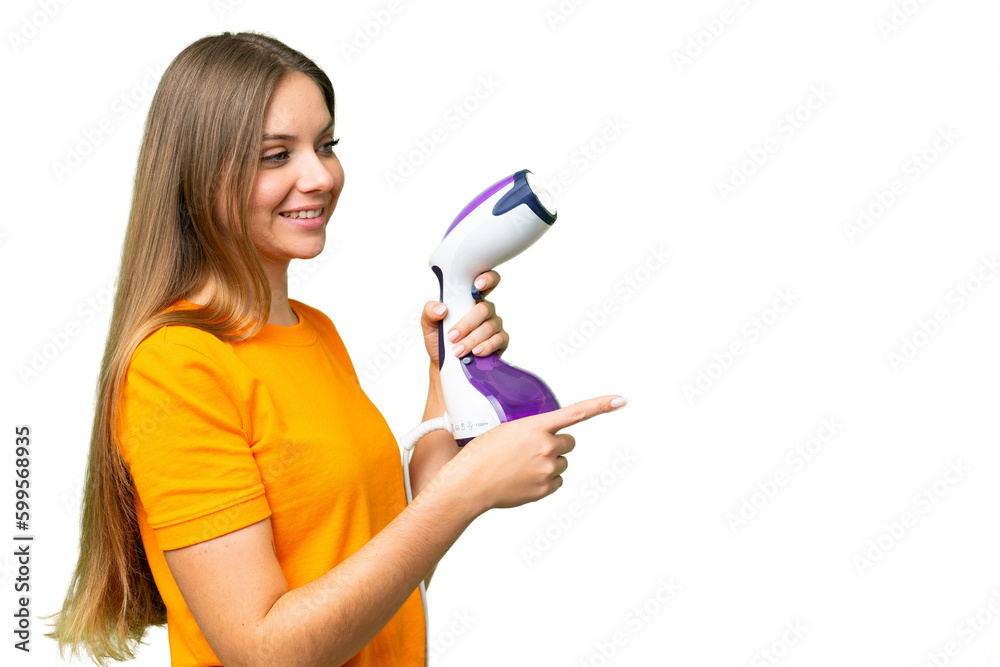 Young blonde woman holding a vertical steam iron over isolated chroma key background pointing to the side to present a product Young blonde woman holding a vertical steam iron over isolated chroma key background pointing to the side to present a product