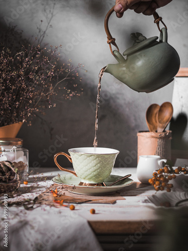 Pouring tea in to green ceramics cup on the table. Selective focus, conceptual stilllife darkmood photography
