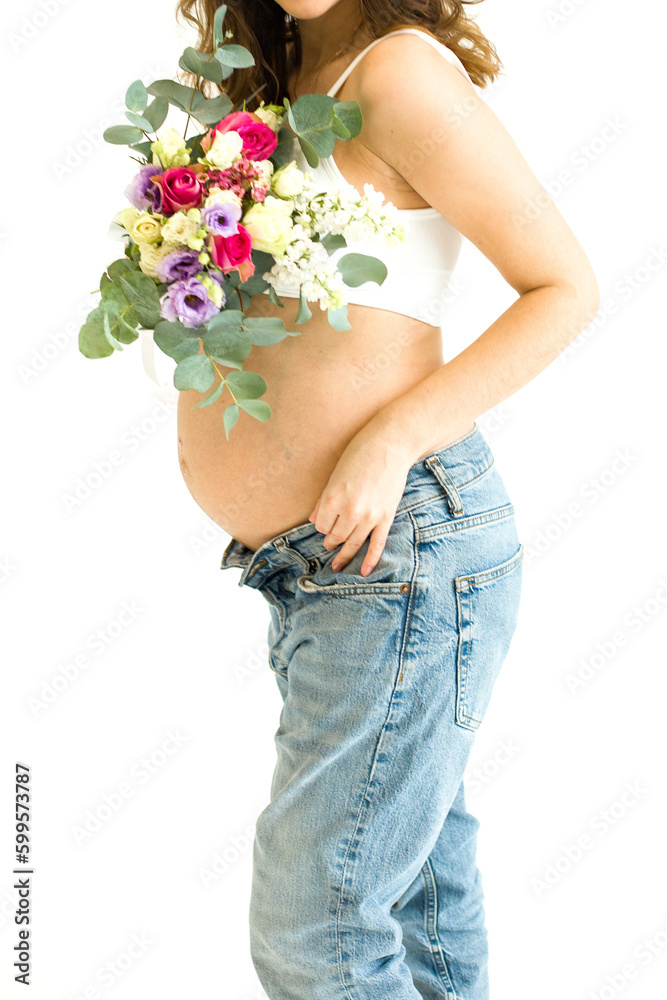 A pregnant woman with flowers in her hands on a white background. Pregnant belly close-up. Pregnancy. Happy Pregnancy Concept. Expectant Mother-To-Be Touching Belly on a white background