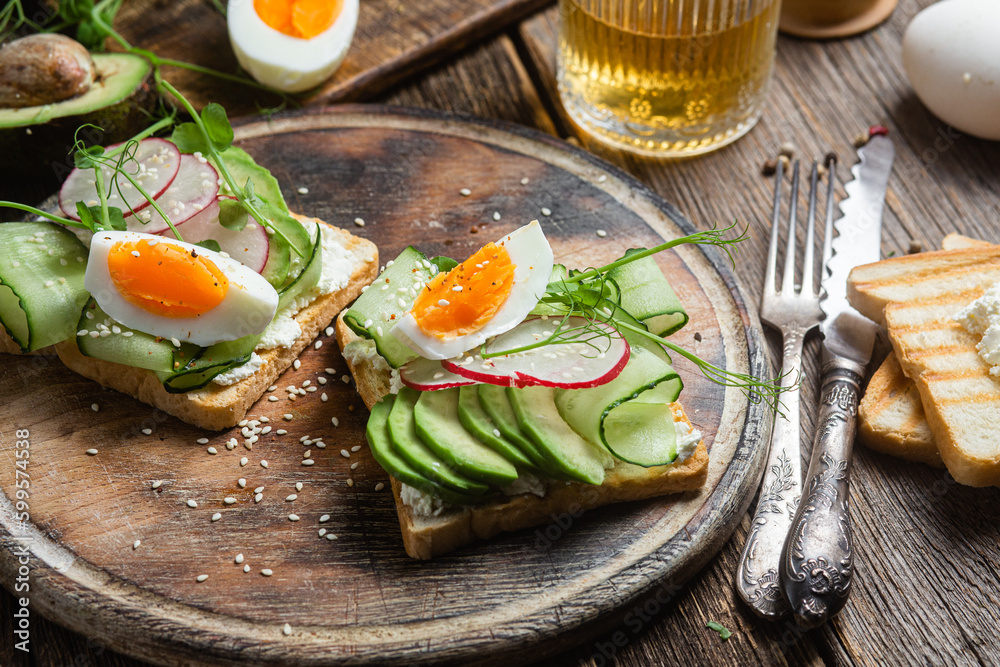 White bread toasts with cream cheese, egg, avocado, cucumber and radish in a plate