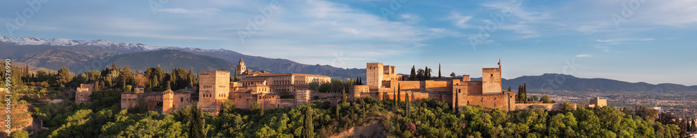 Panoramic sunset hour time of Alhambra medieval palace and fortress complex with Sierra Nevada snowy mountains in Granada, Andalusia, Spain. Known as a Capital of Nasrid Kingdom or Emirate of Granada.