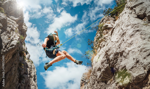 Climber teenage boy in protective helmet jumping on vertical cliff rock wall using rope Belay device, climbing harness in Paklenica canyon in Croatia. Active extreme sports time spending concept