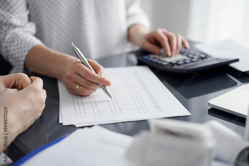 Woman accountant using a calculator and laptop computer while counting taxes for a client. Business audit and finance concepts Woman accountant using a calculator and laptop computer while counting taxes for a client. Business audit and finance concepts