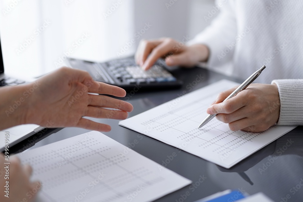 Woman accountant using a calculator and laptop computer while counting taxes for a client. Business audit and finance concepts Woman accountant using a calculator and laptop computer while counting taxes for a client. Business audit and finance concepts