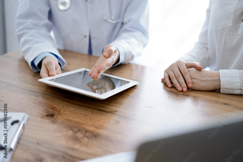 Doctor and patient sitting at the wooden desk in clinic. Female physician's hands pointing into laptop computer monitor, close up. Medicine concept Doctor and patient sitting at the wooden desk in clinic. Female physician's hands pointing into laptop computer monitor, close up. Medicine concept