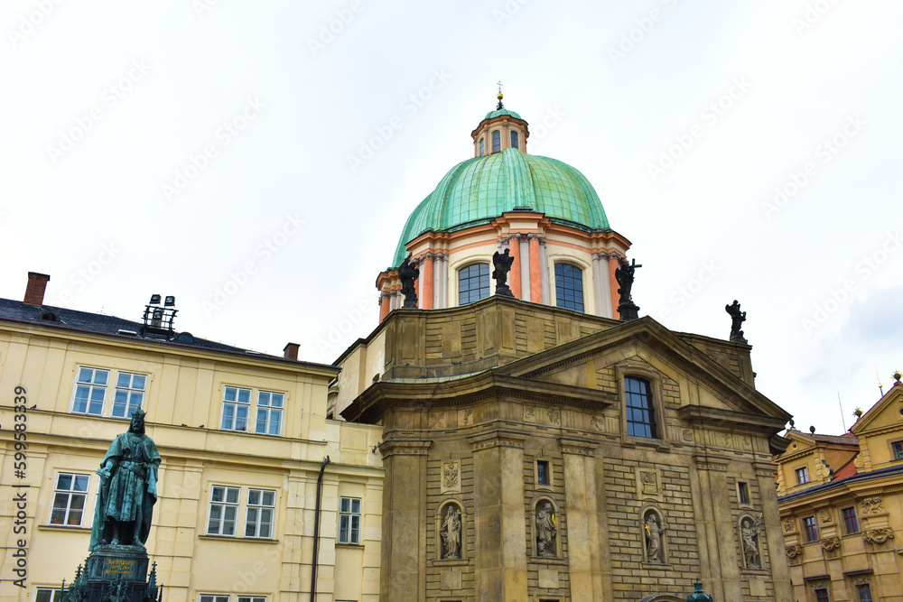 Old building with sculptures on the facade and with a large green dome. An ancient sculpture near the building. Prague, Czech Republic, October 2022.