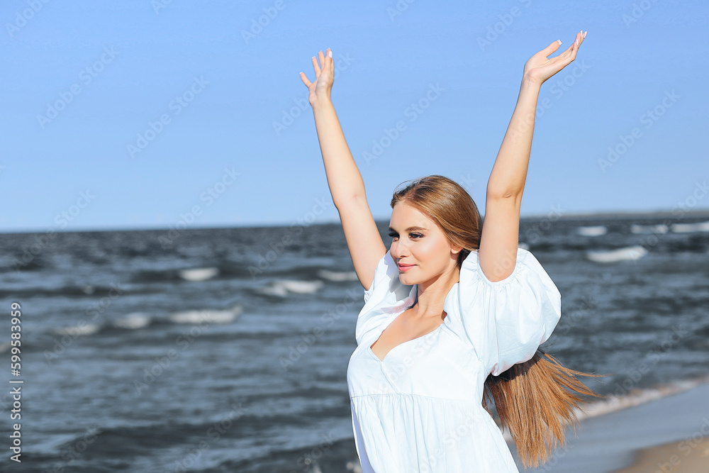 Happy blonde woman is on the ocean beach in a white dress and sunglasses, raising hands Happy blonde woman is on the ocean beach in a white dress and sunglasses, raising hands
