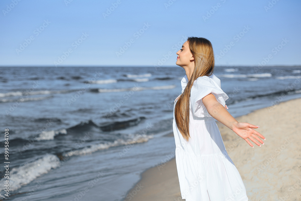 Happy blonde woman is on the ocean beach in a white dress and sunglasses, raising hands Happy blonde woman is on the ocean beach in a white dress and sunglasses, raising hands