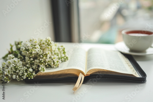 Open bible with flowers and a cup of tea on a white background