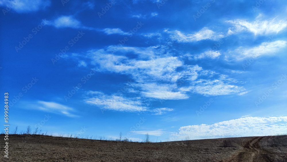 Beautiful blue sky with white clouds on a sunny autumn or spring day over a field with dry grass. Natural Background and copy space. Landscape in early spring or autumn